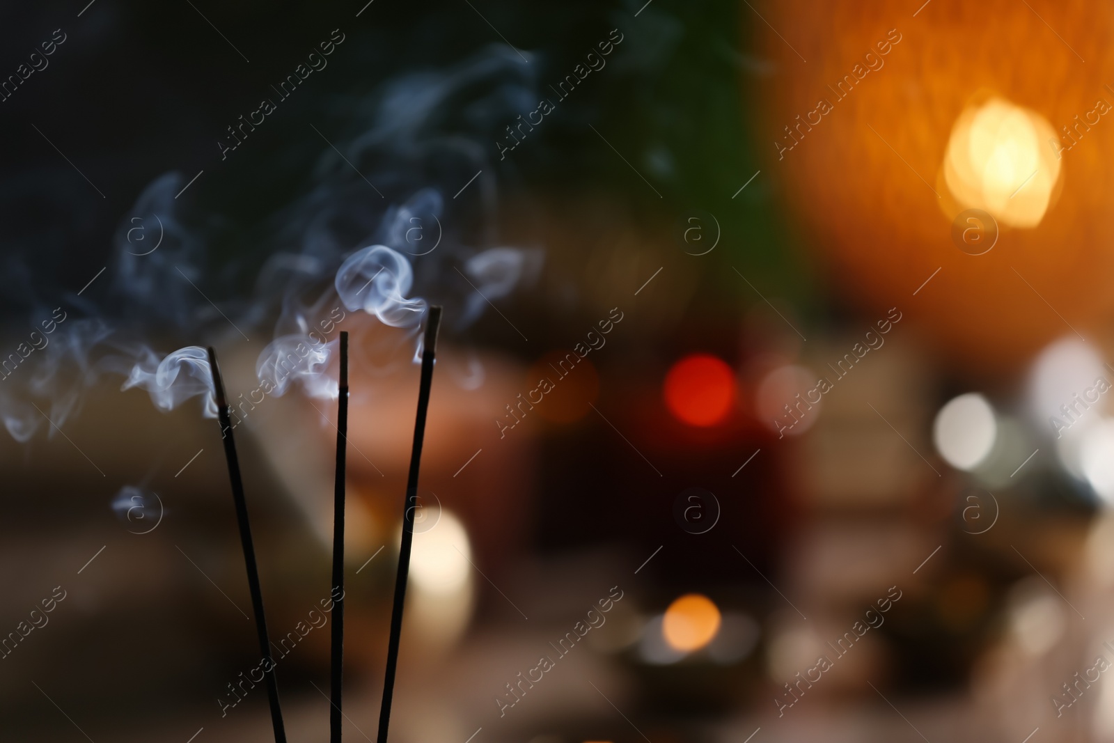 Photo of Incense sticks smoldering on blurred background, closeup. Space for text