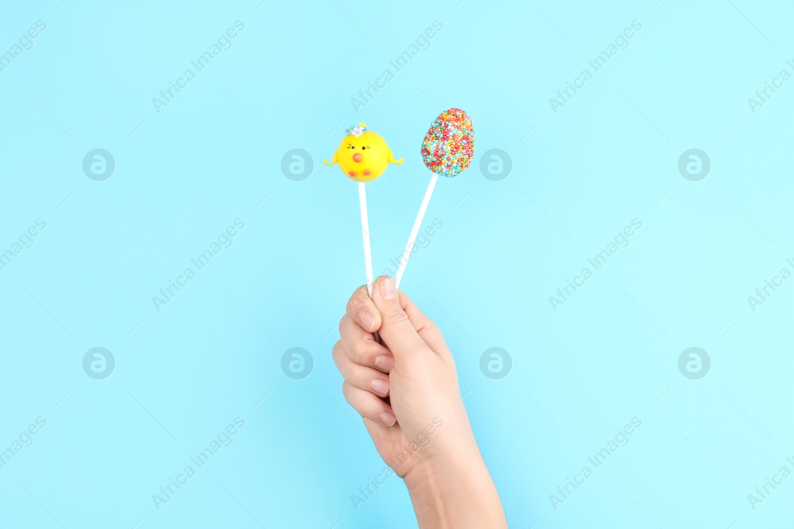 Photo of Woman with delicious cake pops on light blue background, closeup. Easter holiday