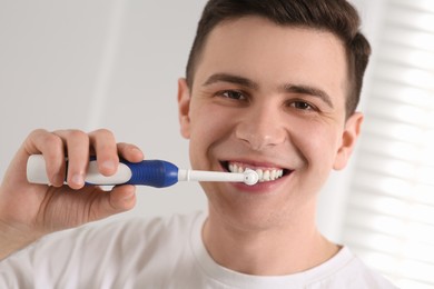 Photo of Man brushing his teeth with electric toothbrush indoors