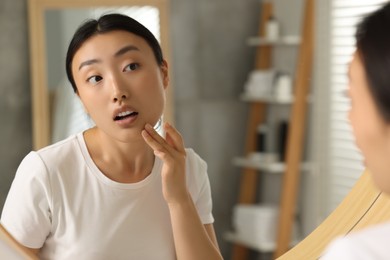 Photo of Suffering from allergy. Young woman checking her face near mirror in bathroom