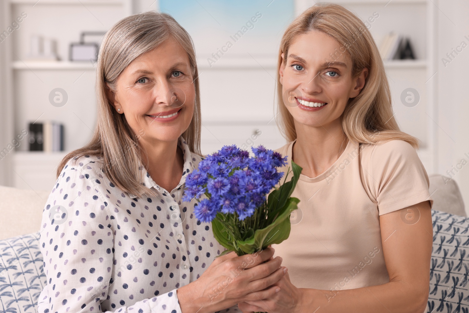 Photo of Happy mature mother and her daughter with beautiful cornflowers at home