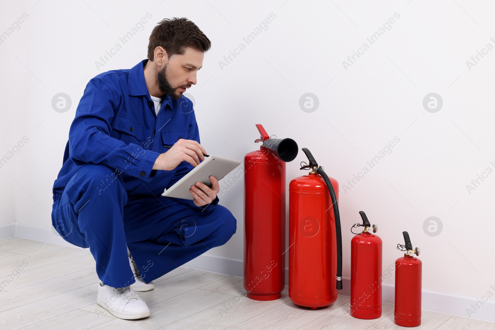 Photo of Man with tablet checking fire extinguishers indoors