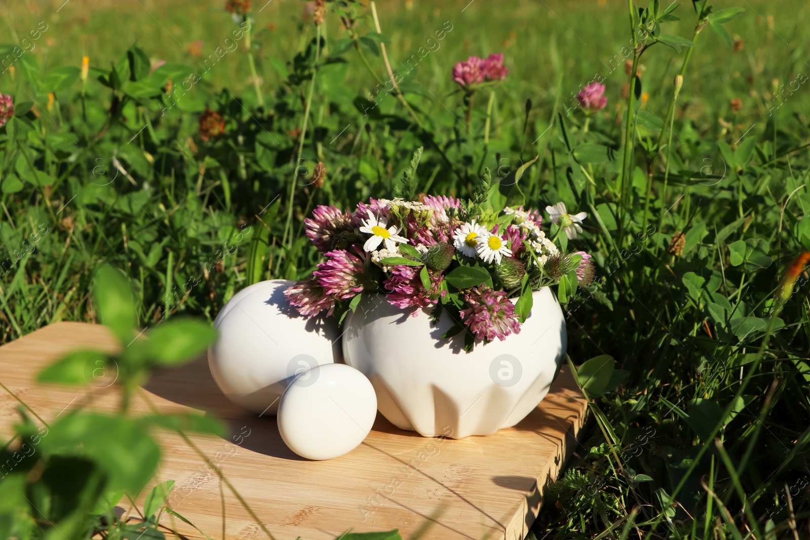 Photo of Ceramic mortar with pestle, different wildflowers and herbs on wooden board in meadow