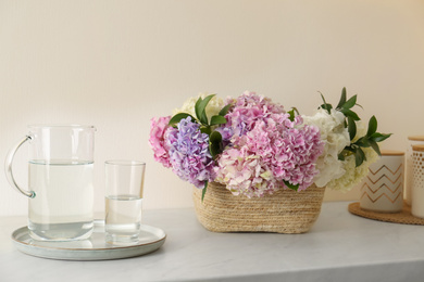 Photo of Beautiful hydrangea flowers in basket and water on light table