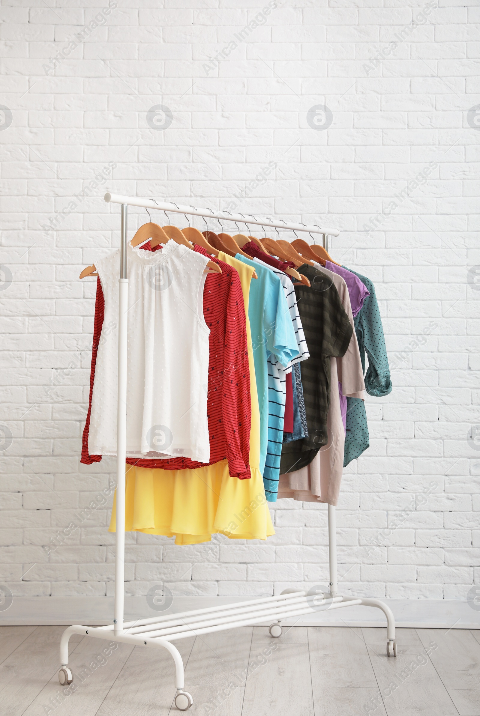 Photo of Wardrobe rack with stylish clothes near brick wall indoors. Space for text