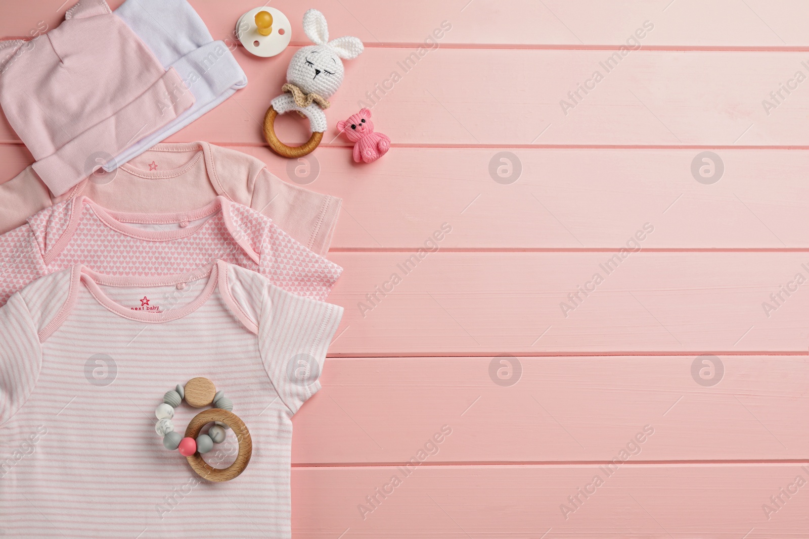 Photo of Flat lay composition with baby clothes and accessories on pink wooden background, space for text
