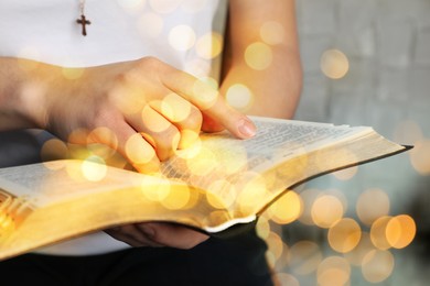 Image of Woman reading Bible near white wall, closeup. Bokeh effect