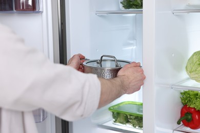 Photo of Man taking pot out of refrigerator in kitchen, closeup