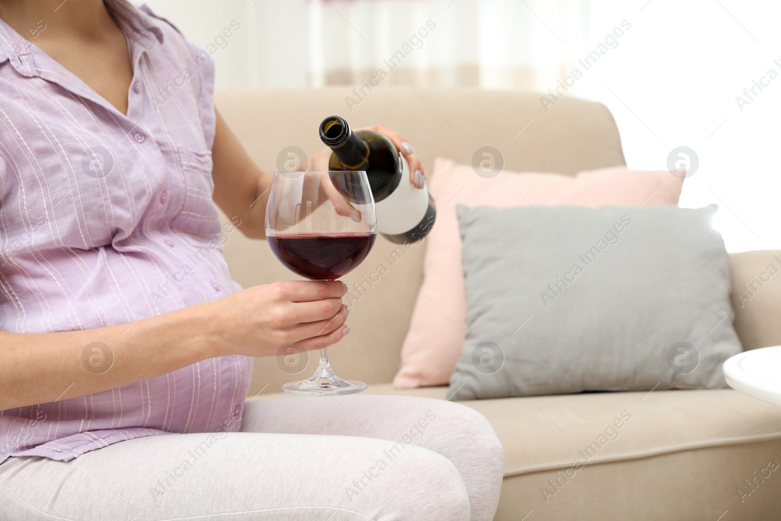 Photo of Future mother pouring wine from bottle into glass at home, closeup. Alcohol abuse during pregnancy