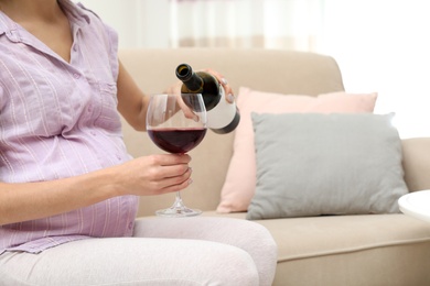 Photo of Future mother pouring wine from bottle into glass at home, closeup. Alcohol abuse during pregnancy