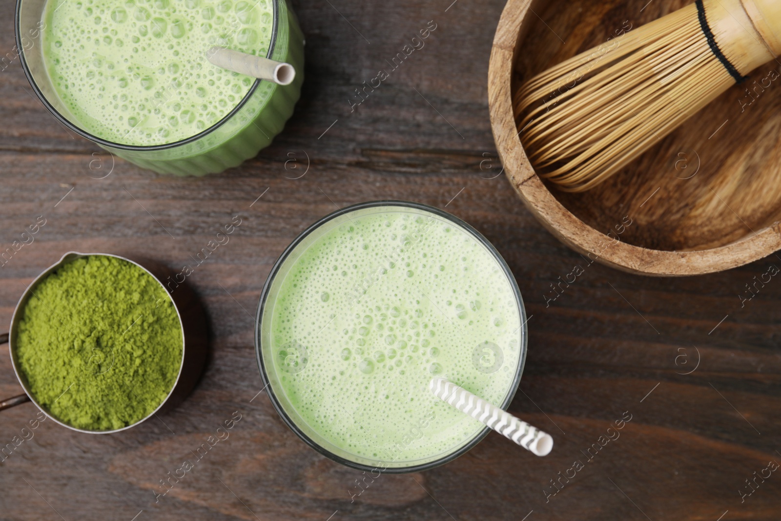 Photo of Tasty matcha smoothie, powder and bamboo whisk on wooden table, flat lay