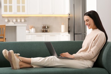 Happy woman working with laptop on sofa in kitchen
