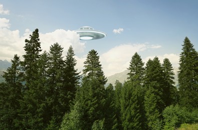 Image of Alien spaceship flying over trees in mountains. UFO