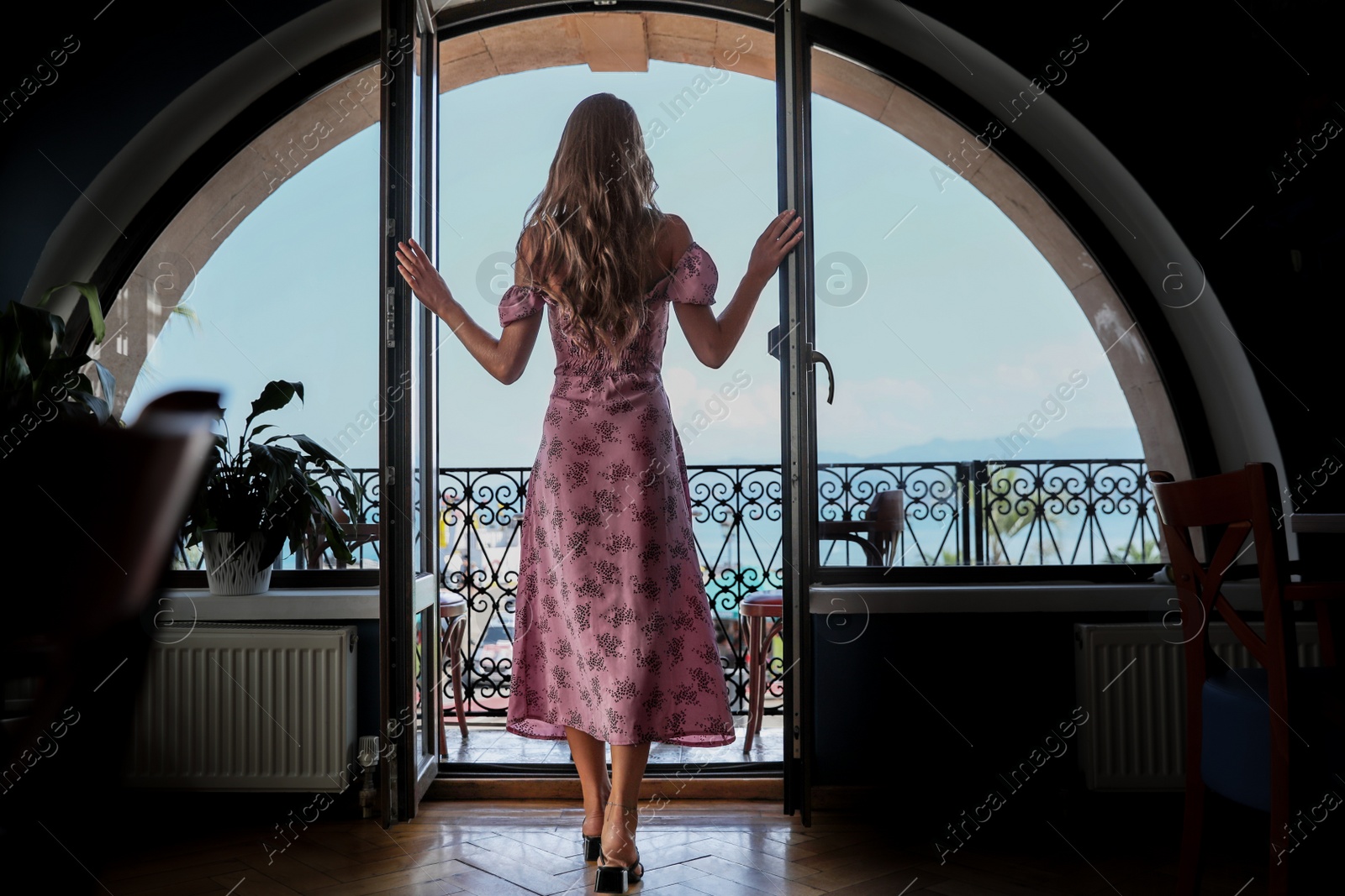 Photo of Young woman standing on balcony, back view