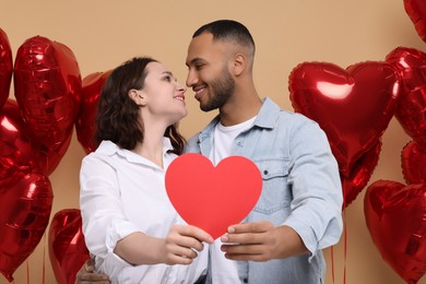 Photo of Lovely couple with red paper heart on beige background. Valentine's day celebration