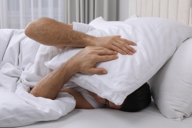 Photo of Handsome man sleeping under pillow in bed at home