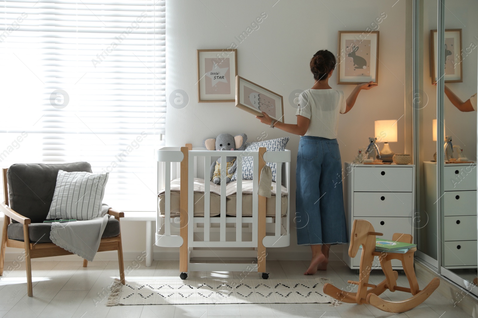 Photo of Decorator hanging pictures on wall in baby room. Interior design