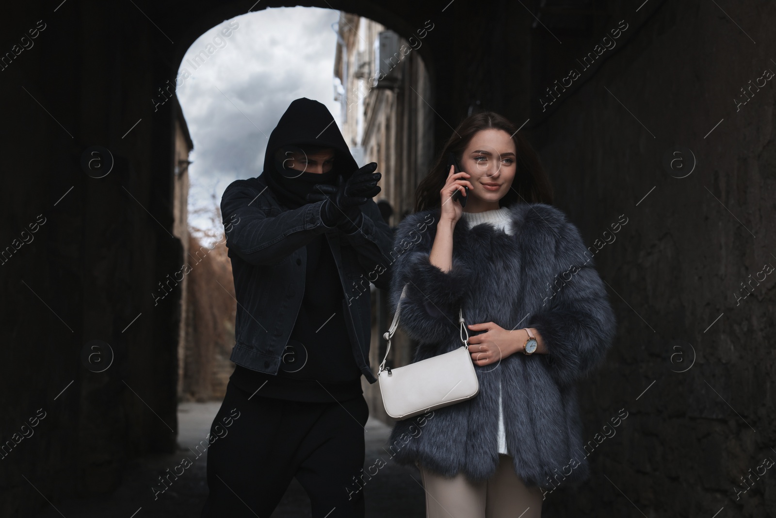 Photo of Criminal attacking young woman while she talking on phone in alley. Self defense concept