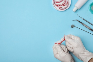 Photo of Dentist holding tooth prosthesis on color background, top view. Space for text