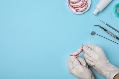 Dentist holding tooth prosthesis on color background, top view. Space for text