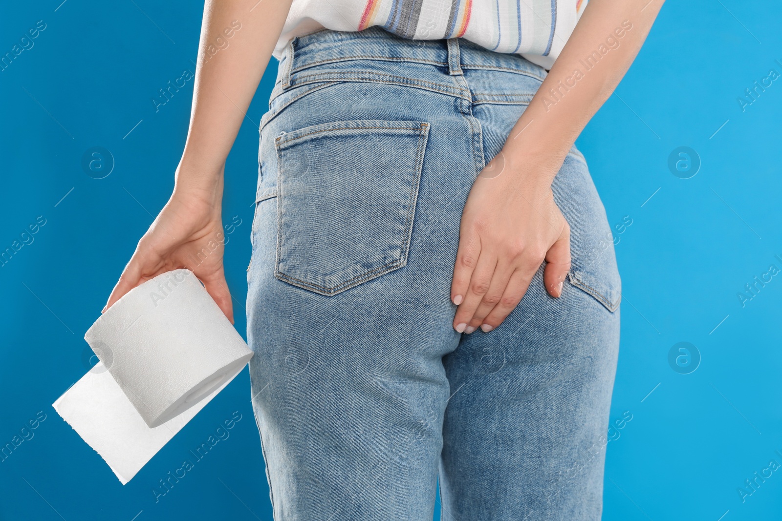 Photo of Woman with toilet paper suffering from hemorrhoid on light blue background, closeup