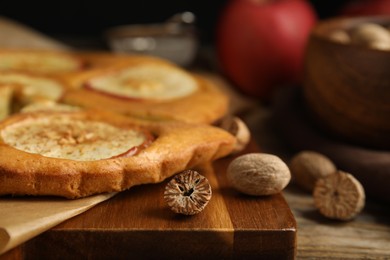 Photo of Nutmeg seeds and tasty apple pie on wooden table, closeup