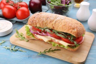 Photo of Delicious sandwich with fresh vegetables, cheese and arugula on light blue wooden table