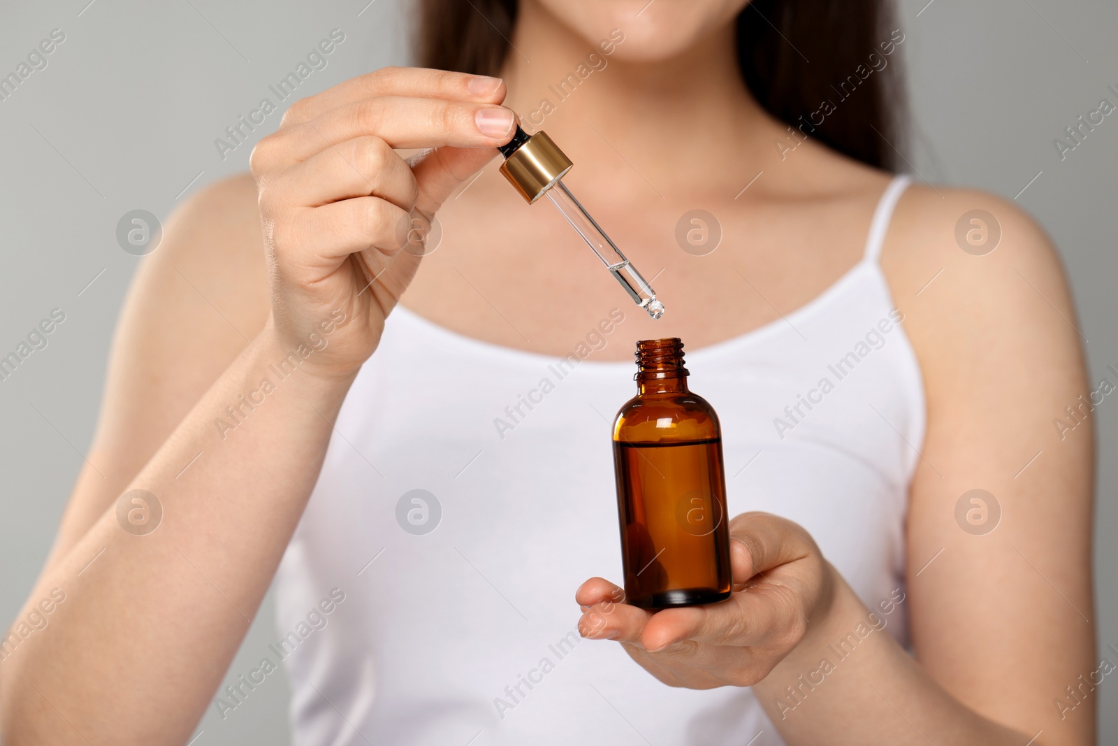 Photo of Beautiful young woman with essential oil on light grey background, closeup