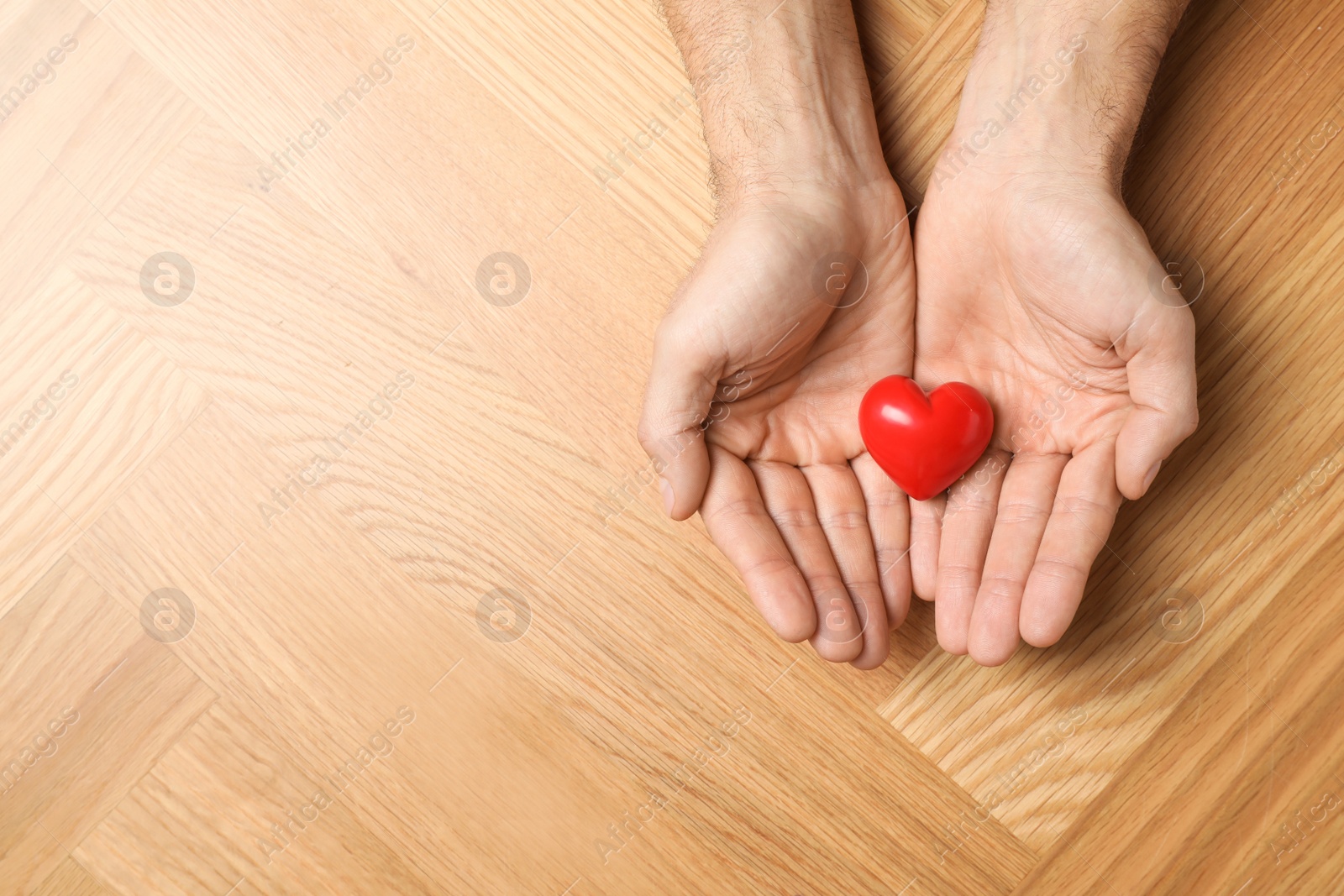 Photo of Man holding red heart in hands at wooden table, top view. Space for text