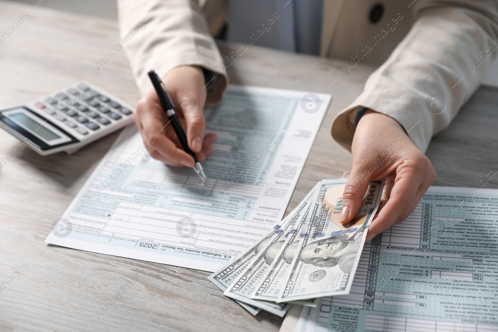 Photo of Payroll. Woman with dollar banknotes working with tax return forms at wooden table, closeup