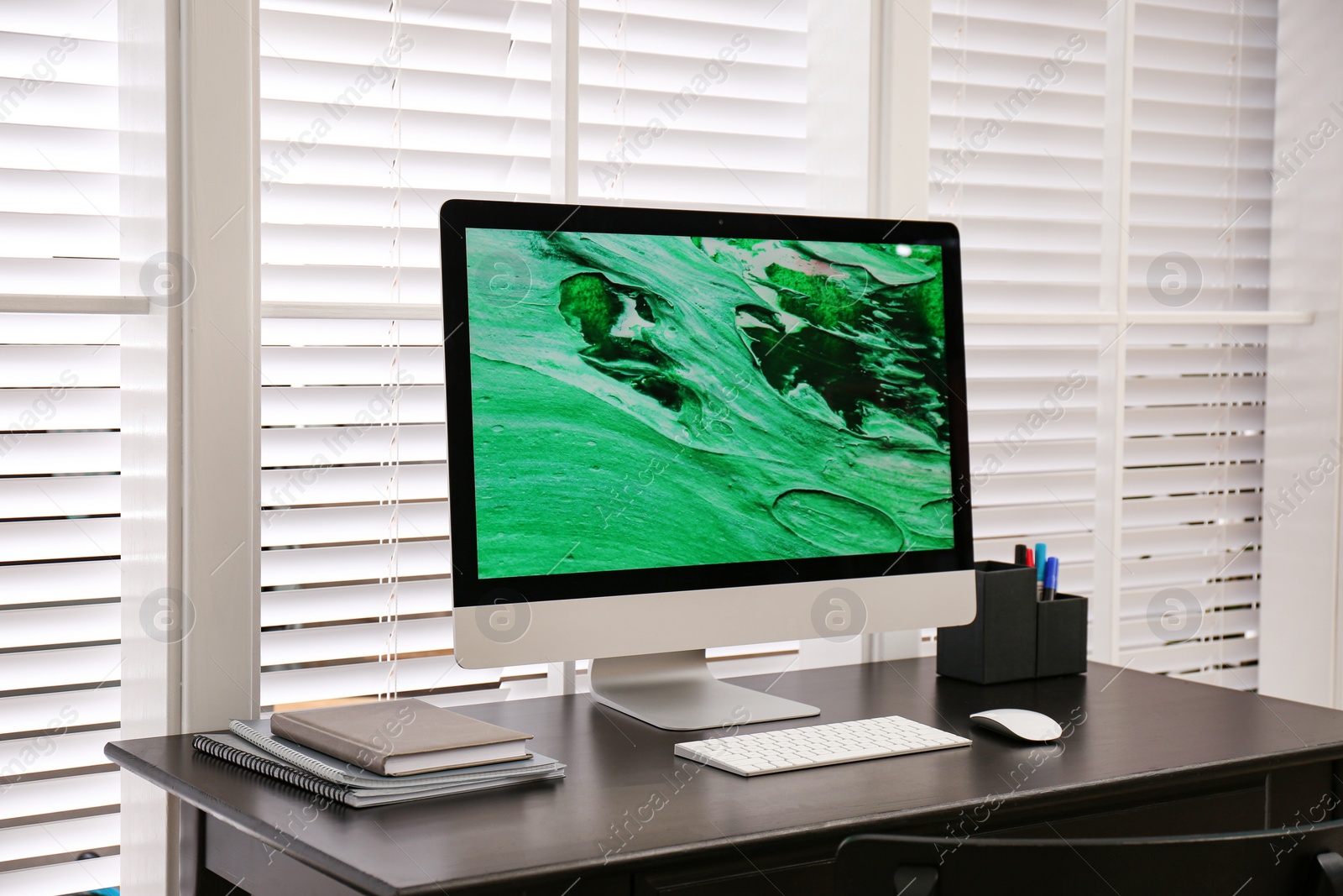 Photo of Comfortable workplace near window with white horizontal blinds in room