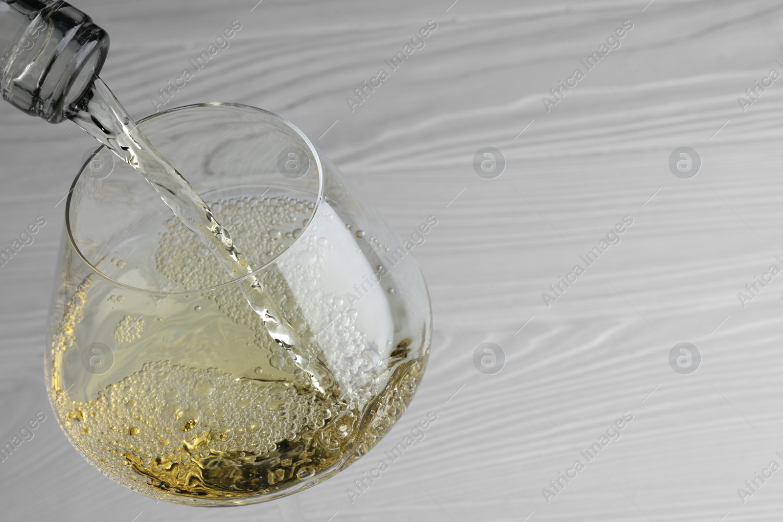 Photo of Pouring tasty aromatic wine in glass at white wooden table, closeup. Space for text