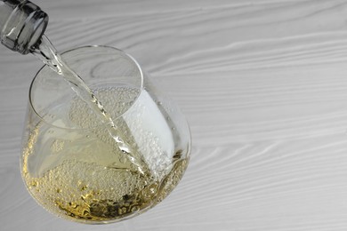 Pouring tasty aromatic wine in glass at white wooden table, closeup. Space for text