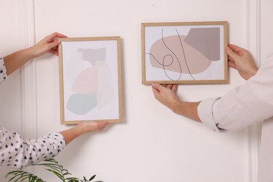 Photo of Man and woman hanging picture frames on white wall, closeup