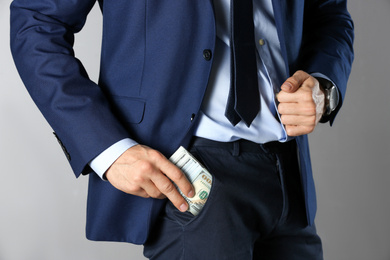 Photo of Man putting bribe into pocket on grey background, closeup