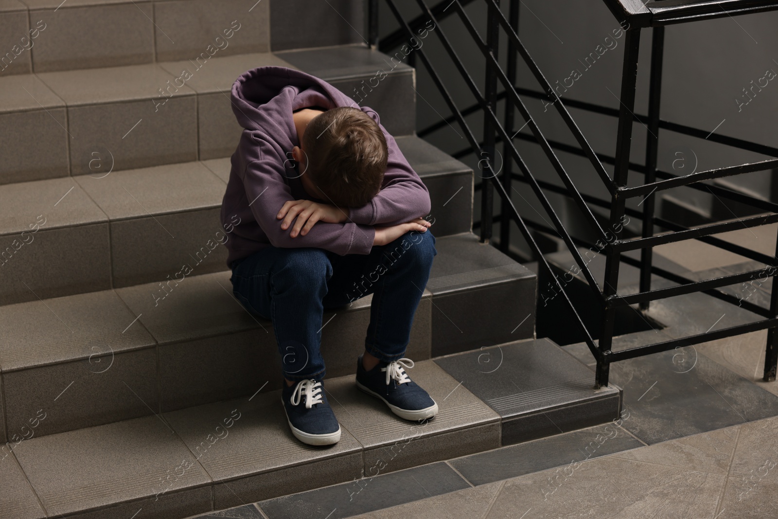 Photo of Child abuse. Upset boy sitting on stairs indoors