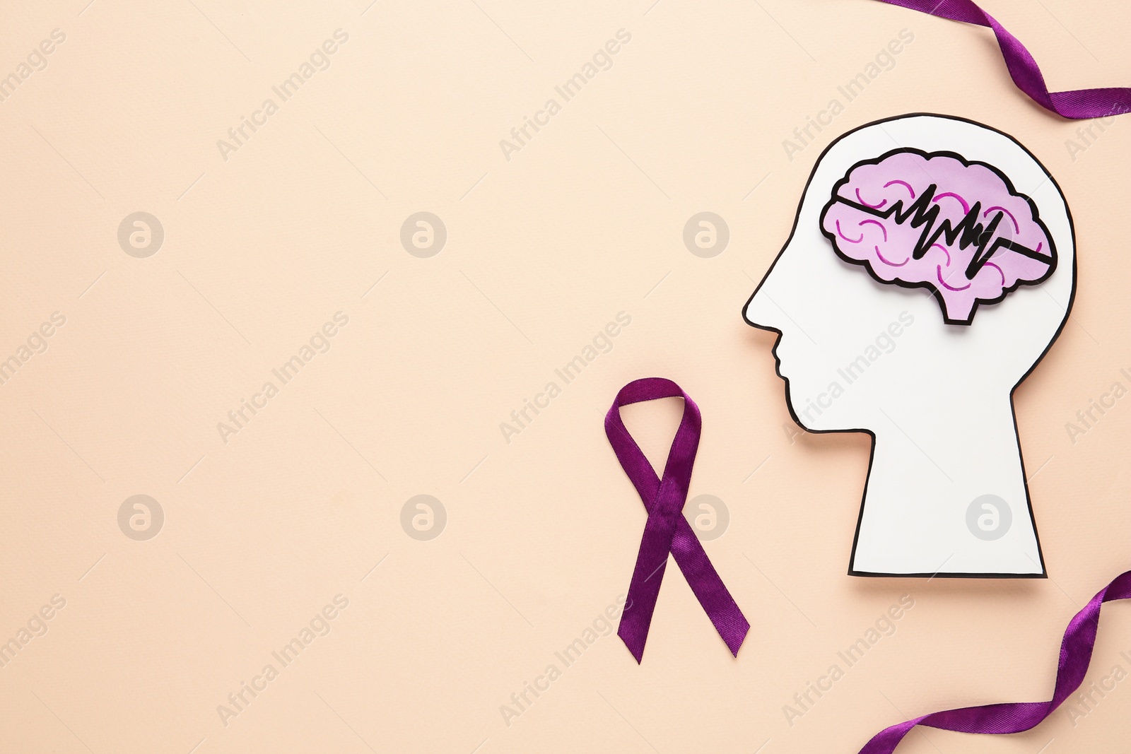 Photo of Human head cutout with brain near purple ribbons on beige background, flat lay. Epilepsy awareness