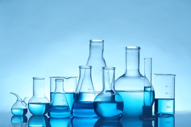Photo of Laboratory glassware with liquid on table against color background. Chemical analysis