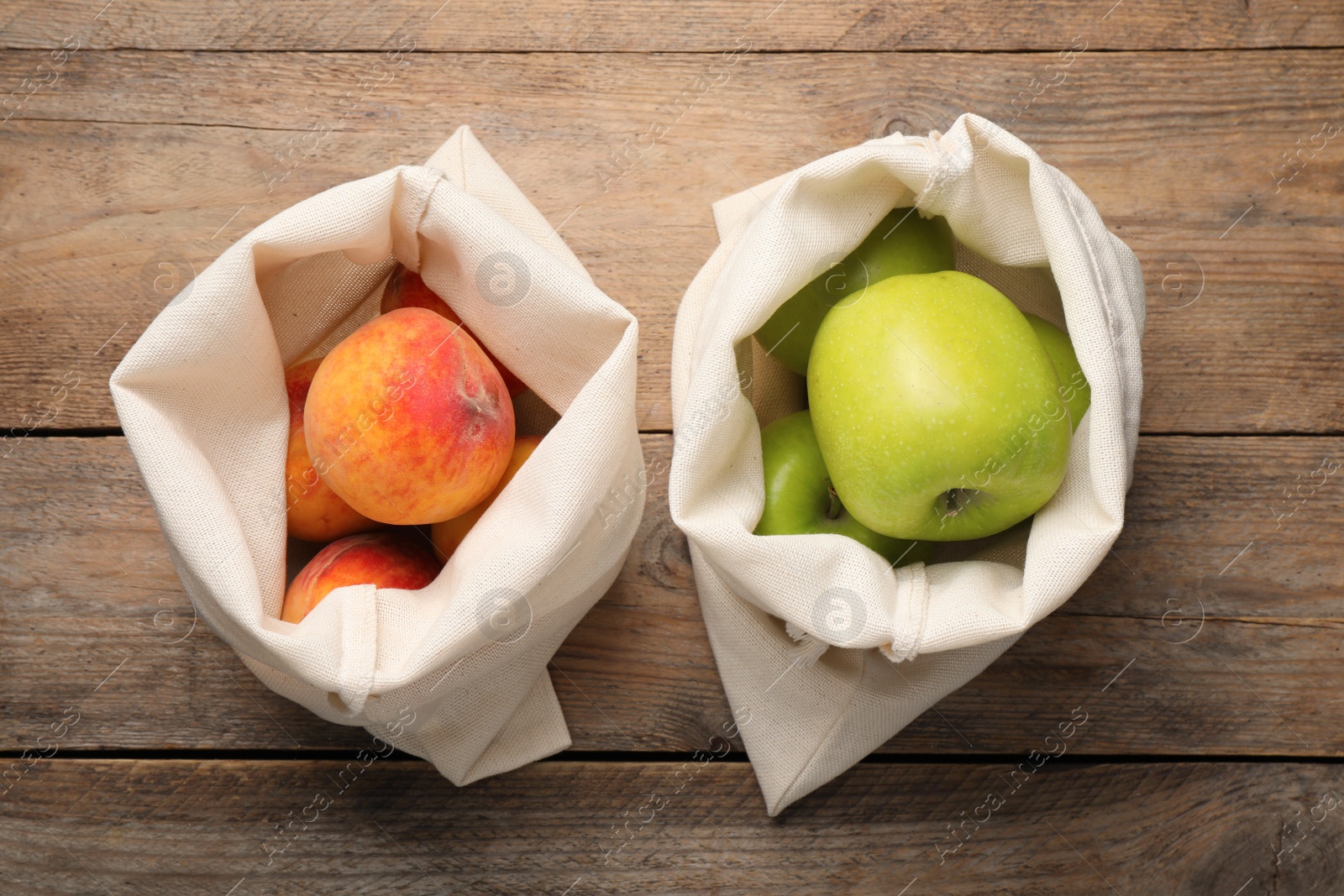 Photo of Sackcloth bags with fresh ripe apples and peaches on wooden table, flat lay