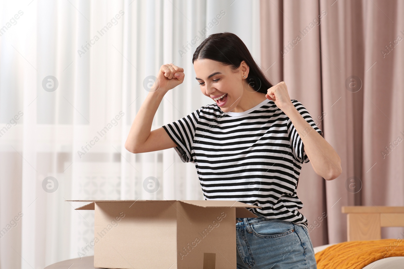 Photo of Emotional young woman opening parcel at home. Internet shopping