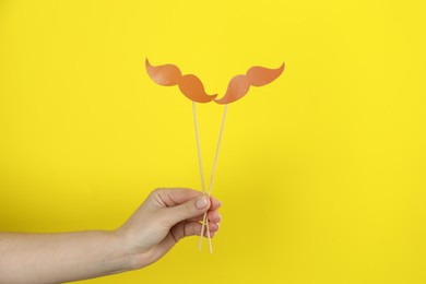 Photo of Woman with fake paper mustaches on yellow background, closeup
