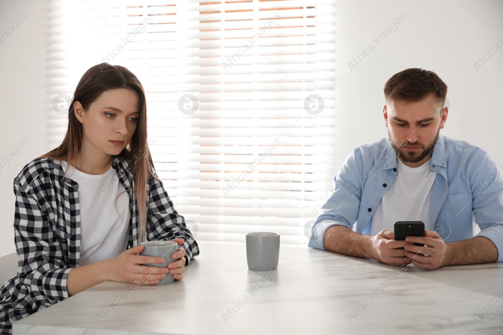 Photo of Young man preferring smartphone over his girlfriend at home. Relationship problems