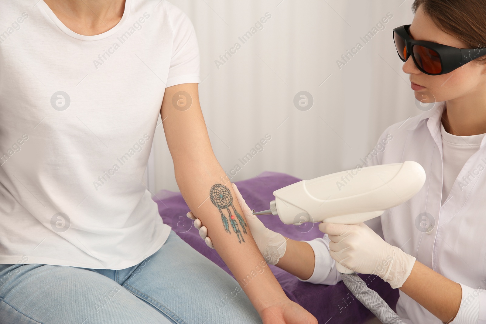 Photo of Young woman undergoing laser tattoo removal procedure in salon