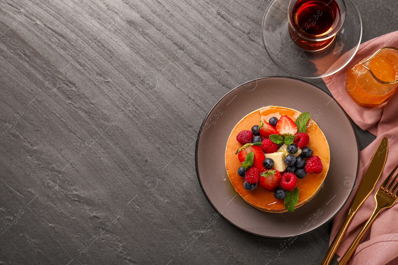 Photo of Delicious pancakes with fresh berries, honey and butter served on grey table, flat lay. Space for text