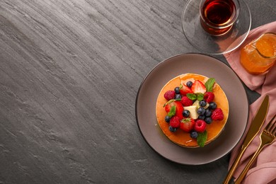 Delicious pancakes with fresh berries, honey and butter served on grey table, flat lay. Space for text