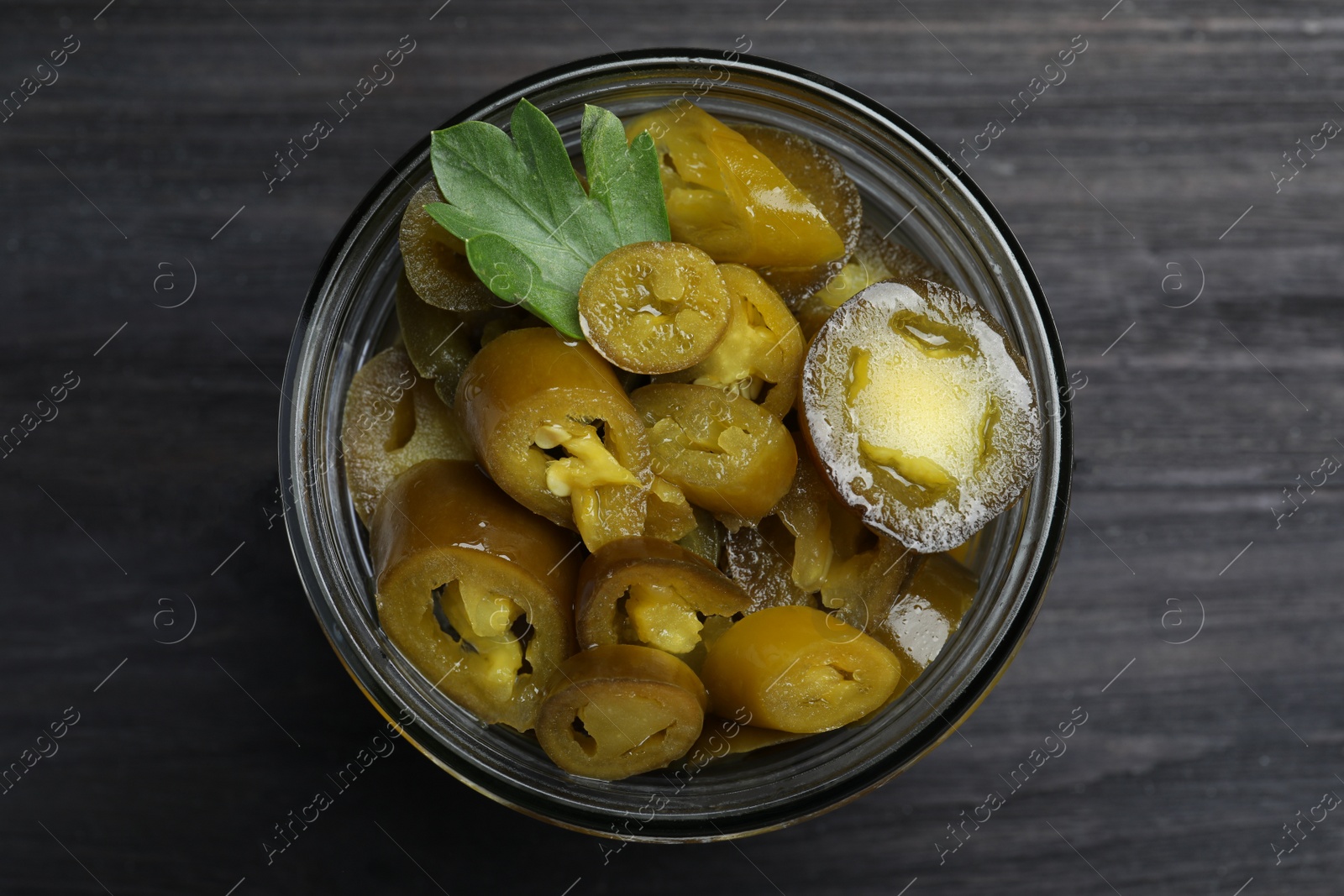 Photo of Glass jar with slices of pickled green jalapeno peppers on black wooden table, top view