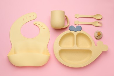 Flat lay composition with baby feeding accessories and bib on pink background