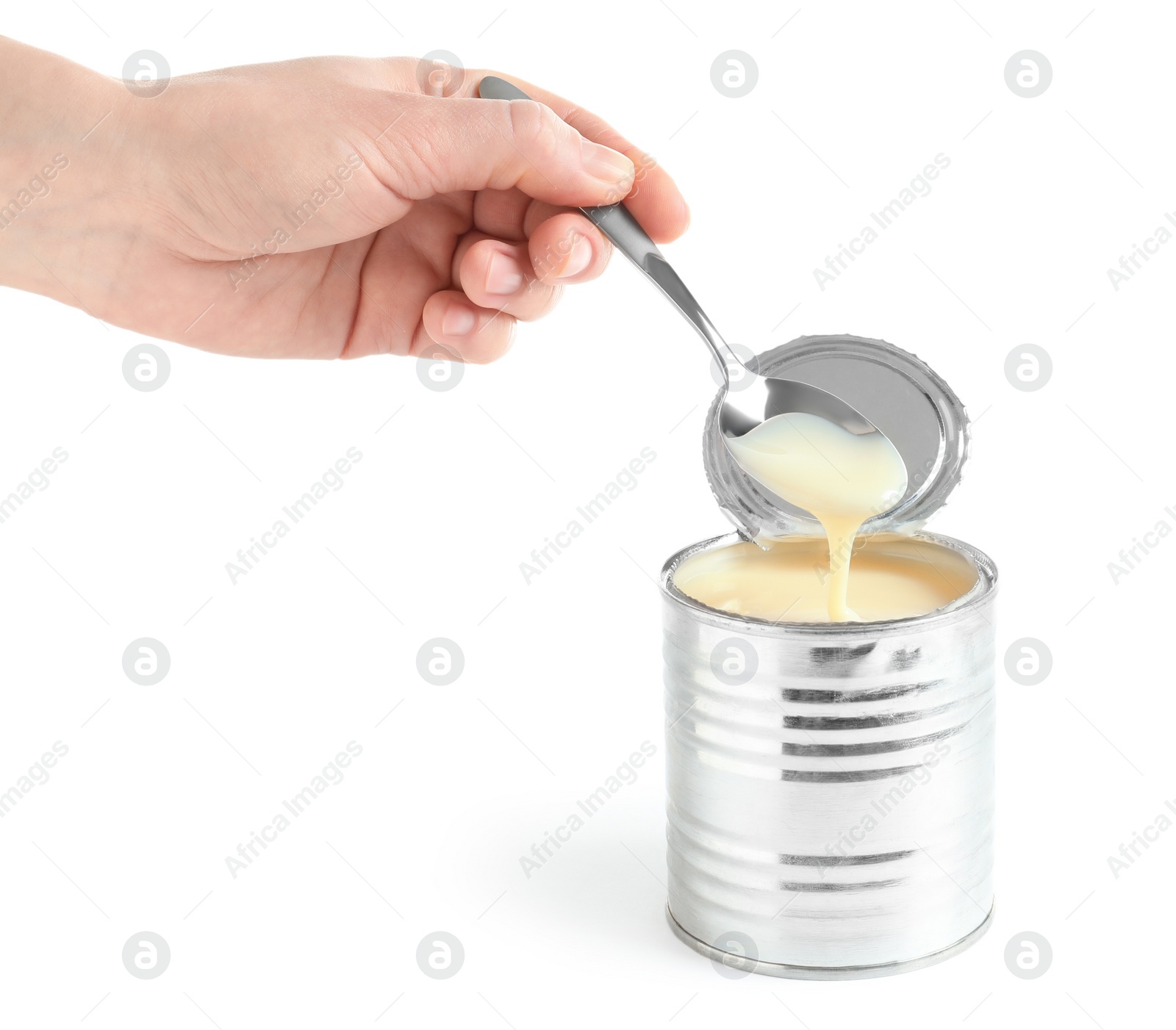 Photo of Woman pouring condensed milk from spoon into tin can on white background, closeup. Dairy product