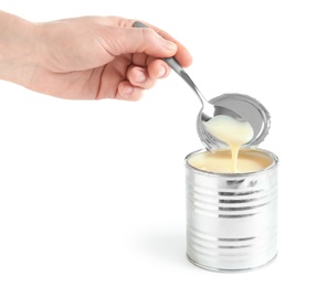 Photo of Woman pouring condensed milk from spoon into tin can on white background, closeup. Dairy product