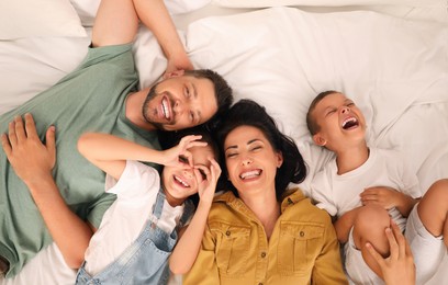 Photo of Happy family with children having fun on bed, top view